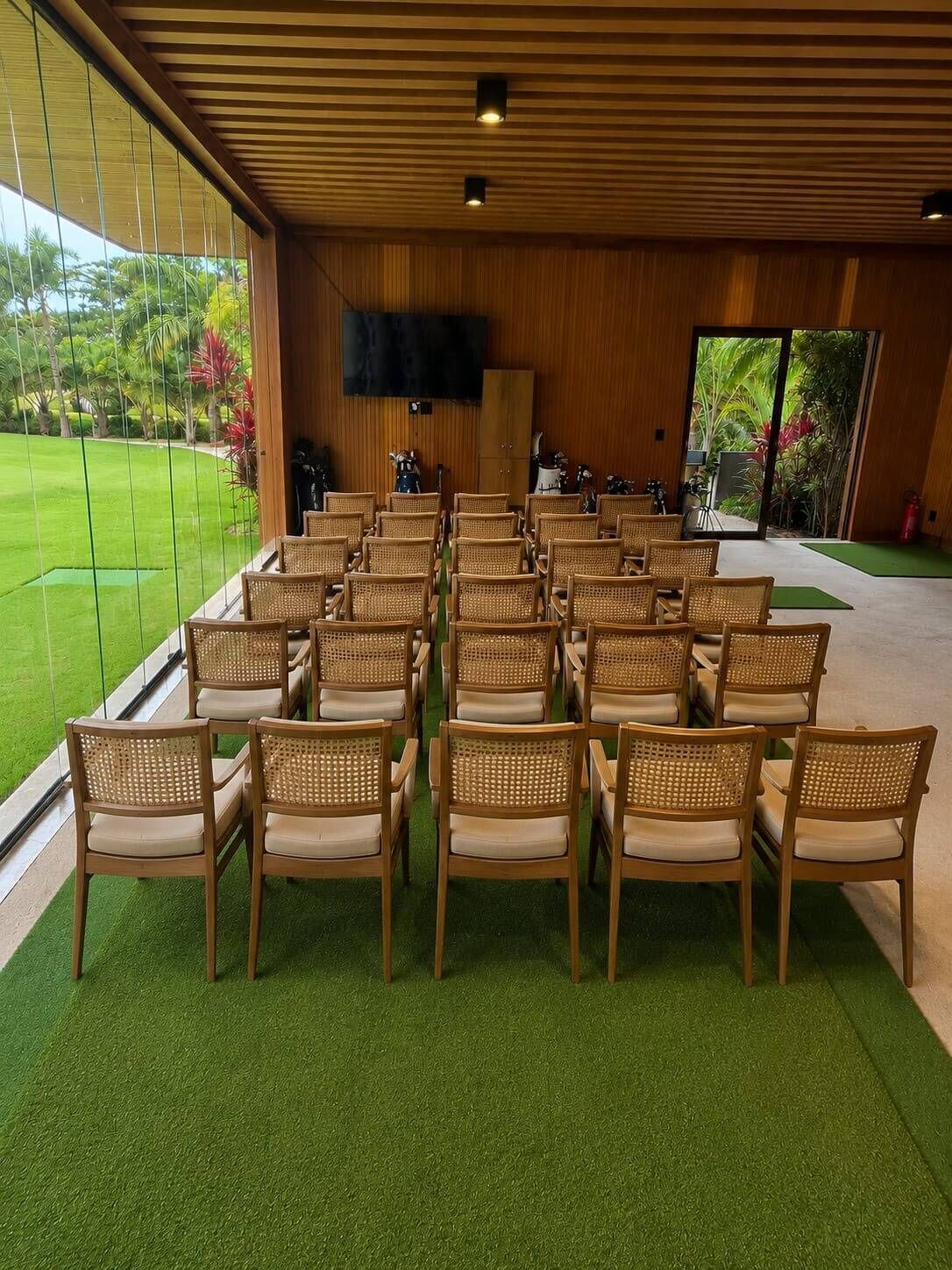 A conference room with rows of wicker chairs, a flat-screen TV, and a view of a well-maintained lawn.