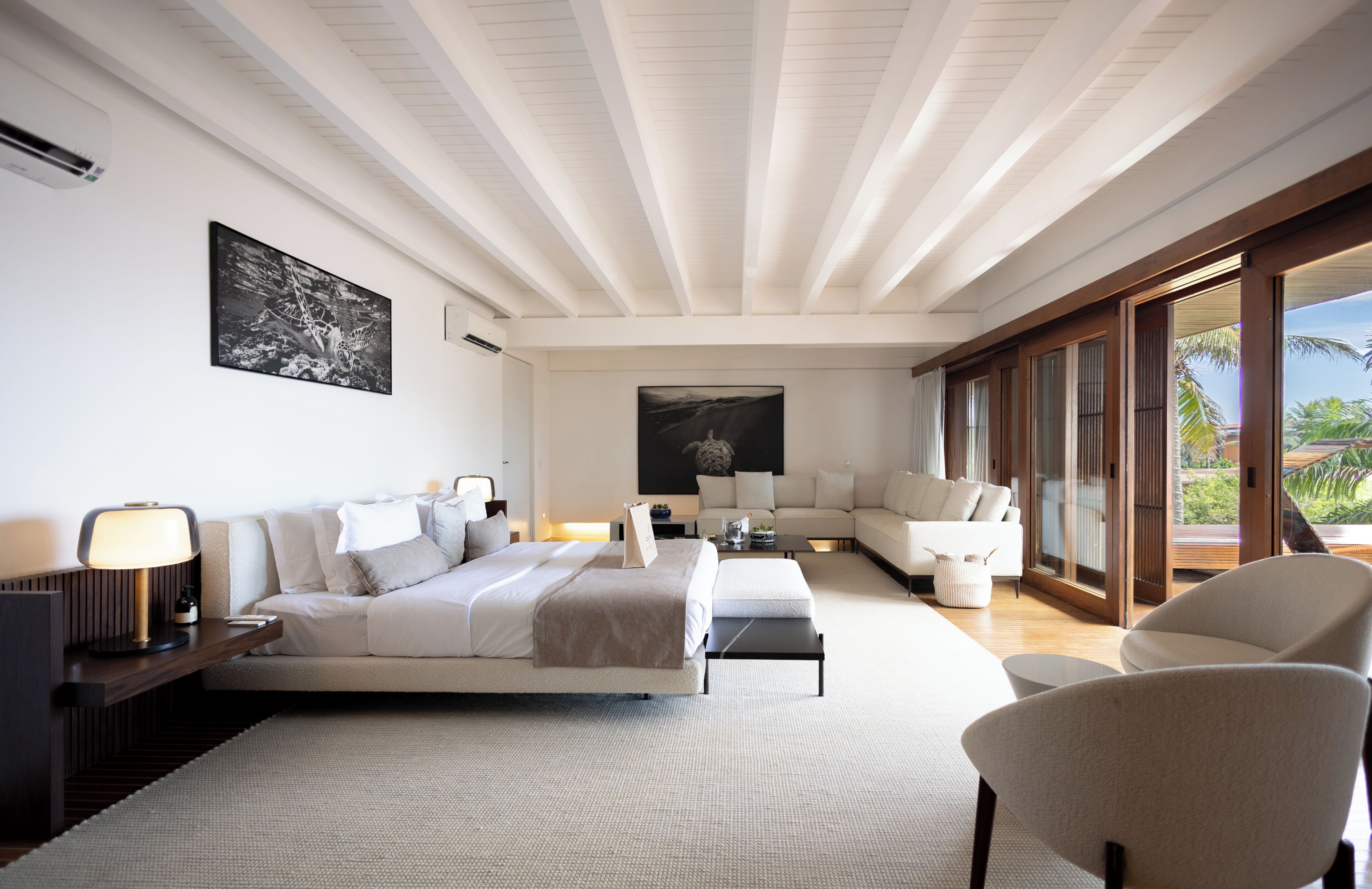 Una habitación de hotel moderna con cama, sofá, sillón y un amplio ventanal con vistas.