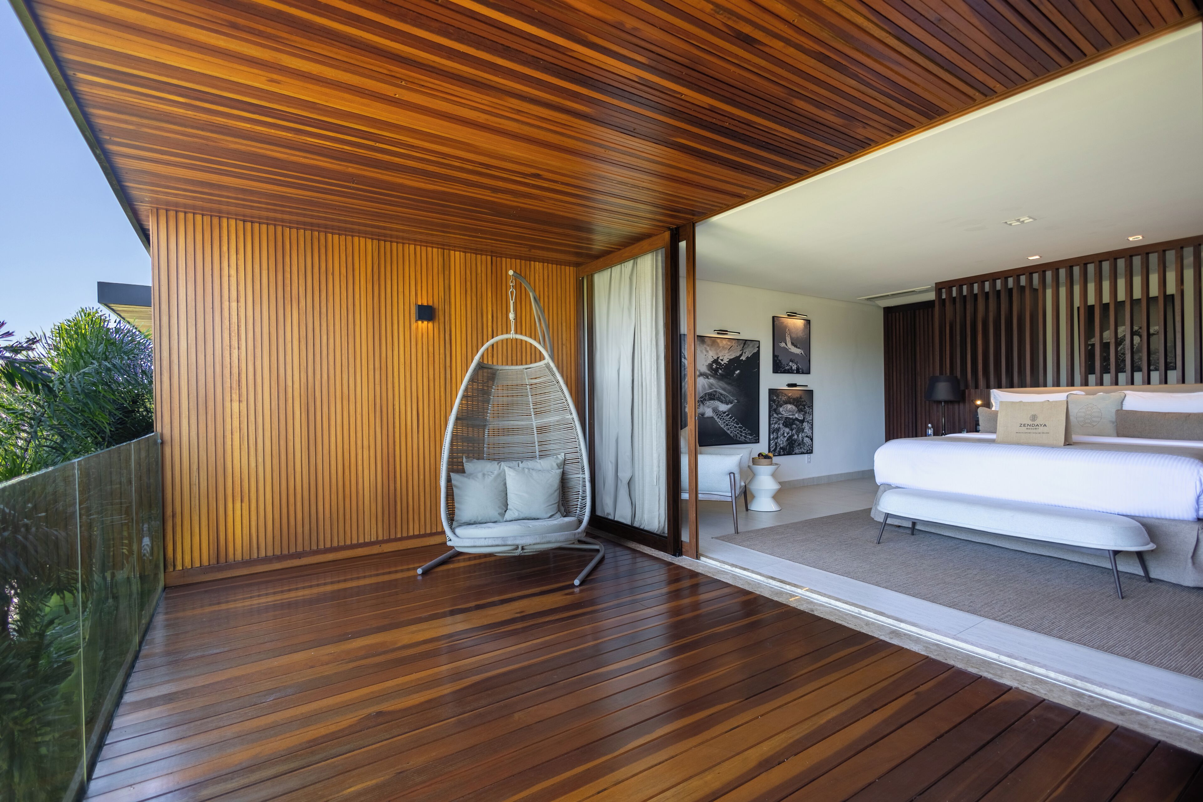 A modern bedroom with a hanging chair, a bed, and a view of the outdoors.