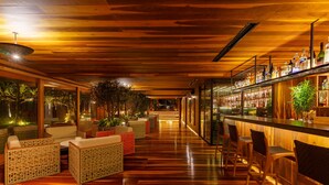 A bar area with wooden flooring, wicker furniture, and a bar stocked with bottles. - Zendaya Resort Beach Sport & Spa (Búzios)