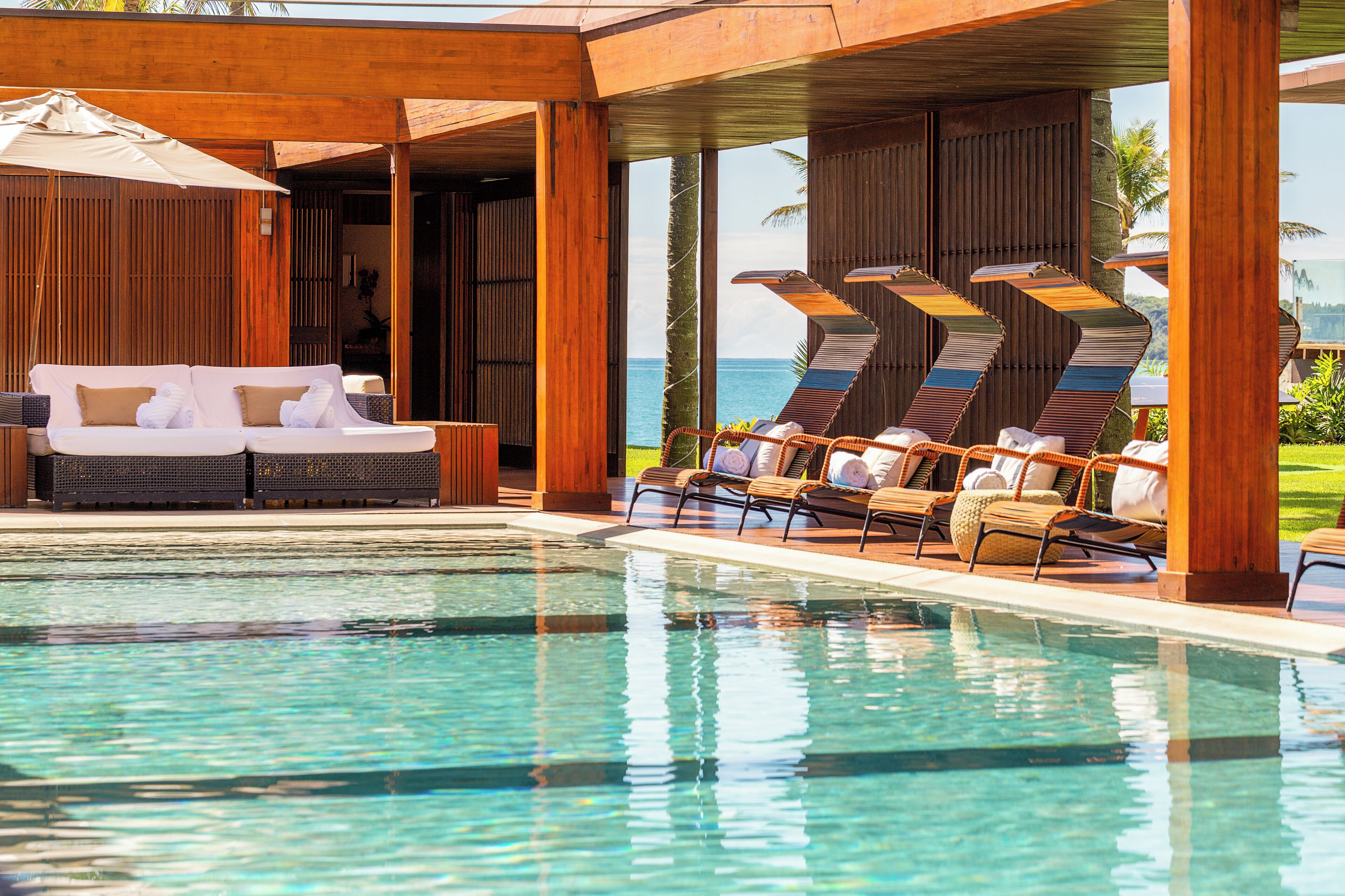 A poolside area with a wooden deck, lounge chairs, and a sofa with towels.