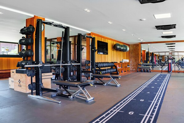 A gym with weightlifting equipment, treadmills, and a mirrored wall.