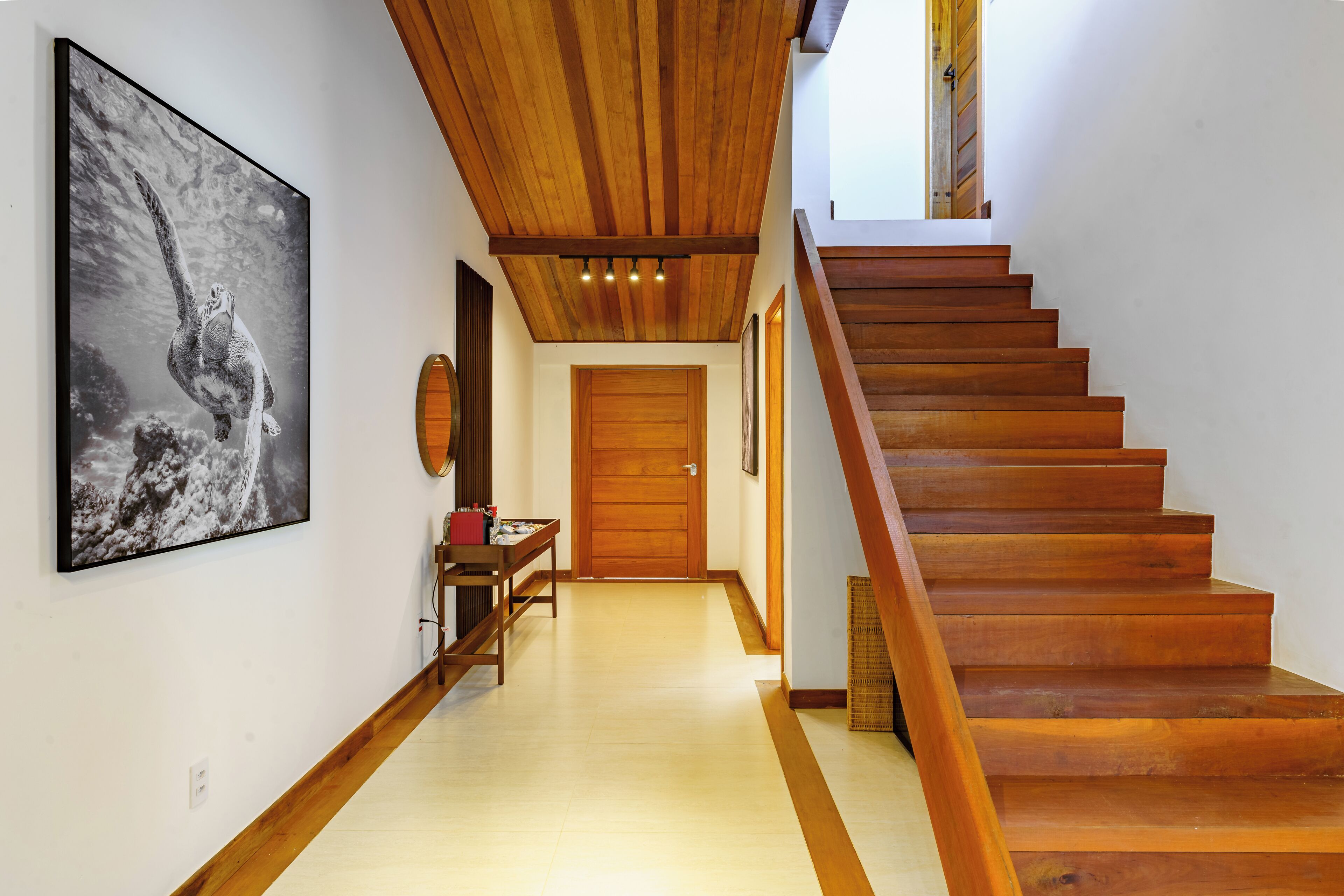A wooden staircase leading to a second floor, a wooden door at the end of a hallway, and a framed picture on the wall.