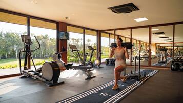 Un gimnasio con equipo de ejercicio y amplias ventanas que dan a zonas verdes.