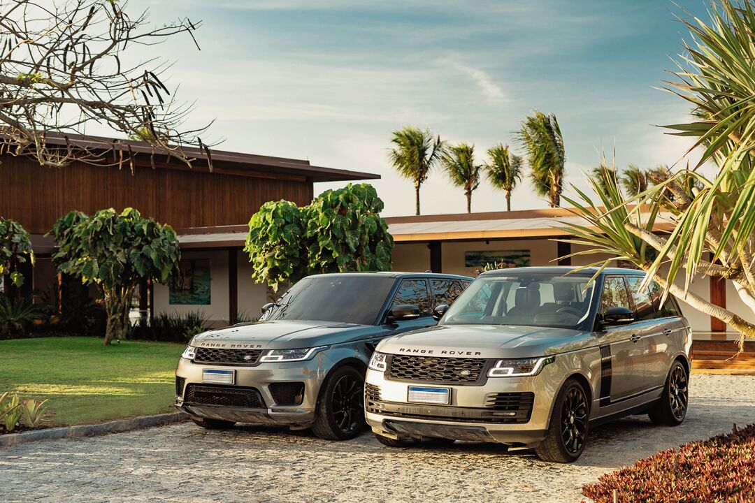Zwei Range Rover Fahrzeuge vor einem modernen Haus mit gepflegtem Rasen und Palmen.