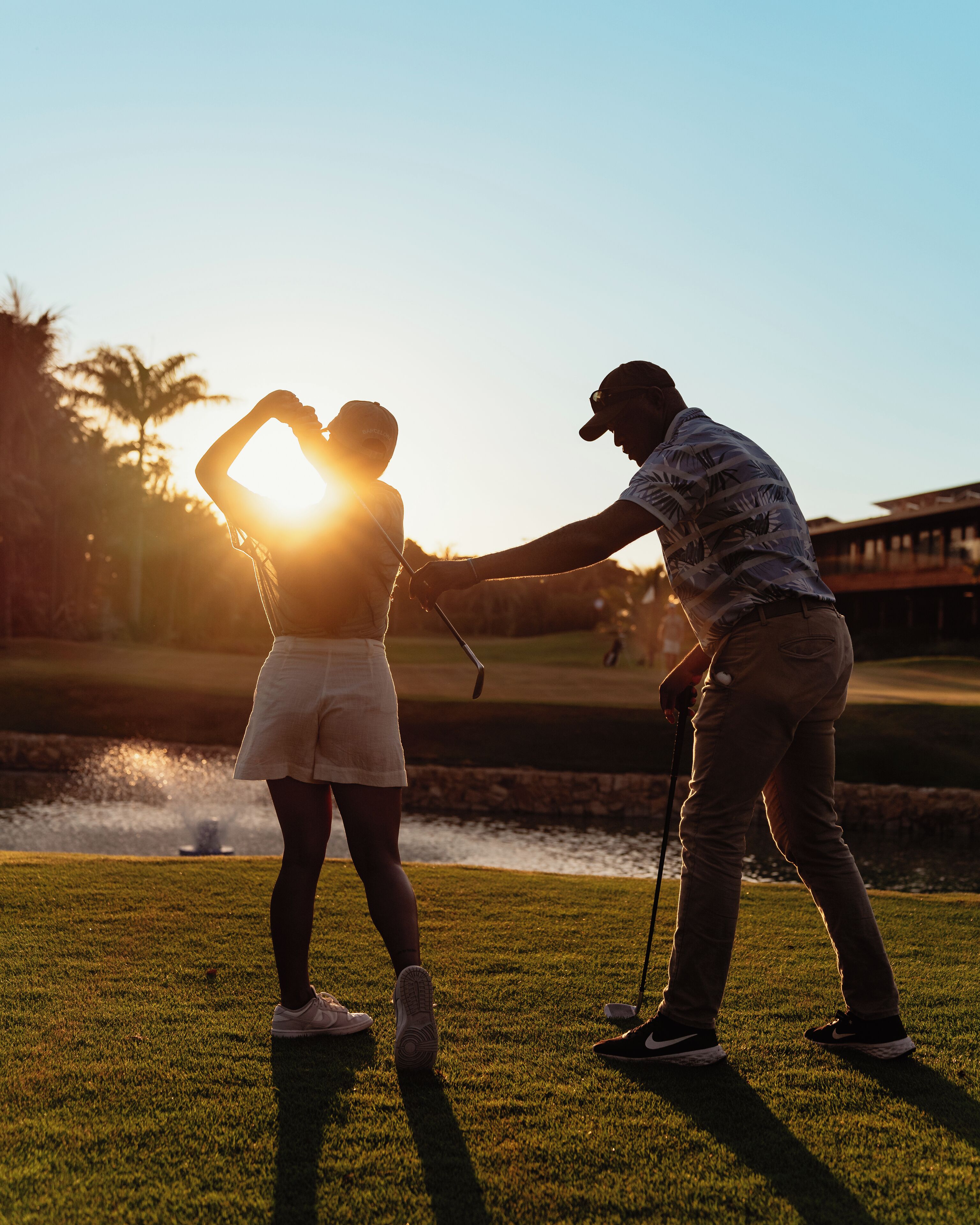 Duas pessoas num campo de golfe, com um obstáculo de água ao fundo.