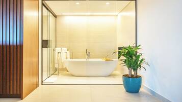 A modern bathroom with a freestanding bathtub, a potted plant, and a glass shower enclosure.