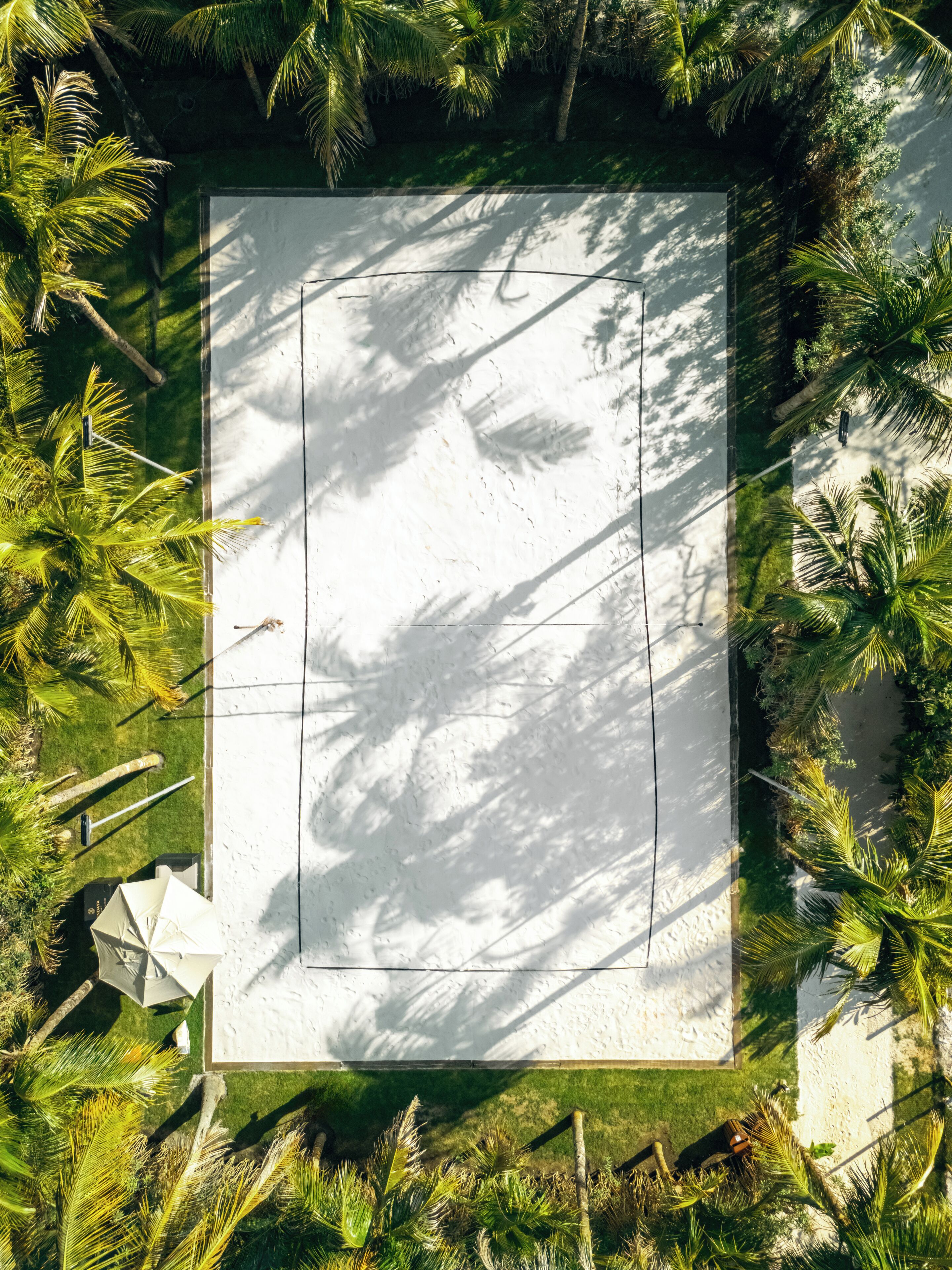 An aerial view of a rectangular area with a white surface, surrounded by palm trees and greenery.