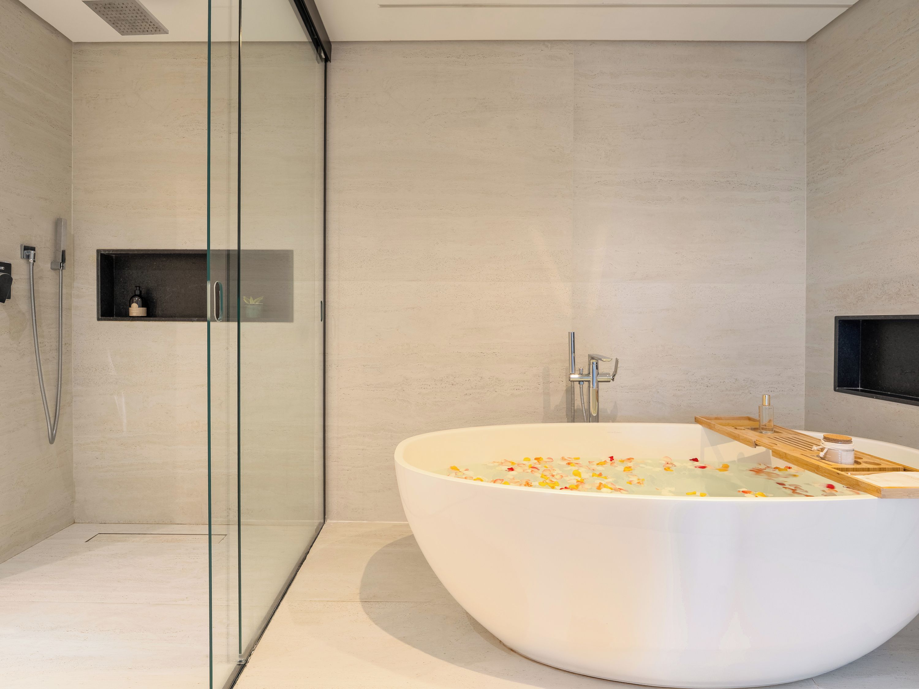 Une salle de bain moderne avec une baignoire sur pieds remplie d’eau et de pétales de rose, une douche à parois de verre et un design minimaliste.