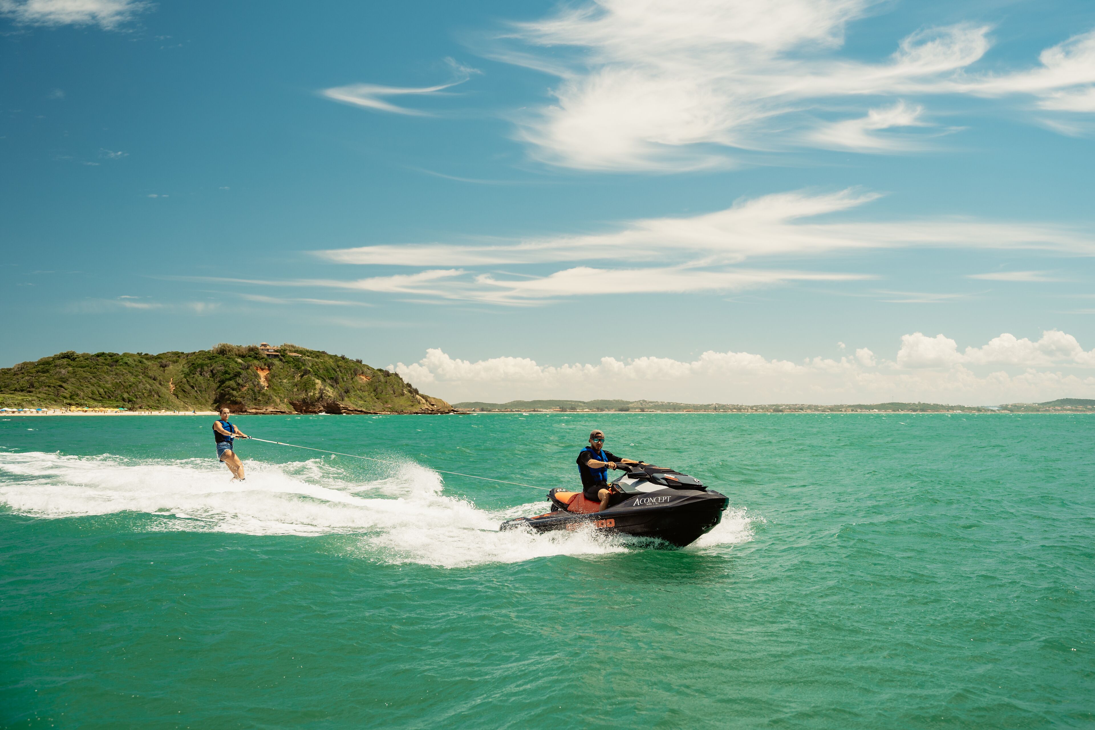 A person water skiing behind a jet ski on turquoise water with a distant island and clear sky.