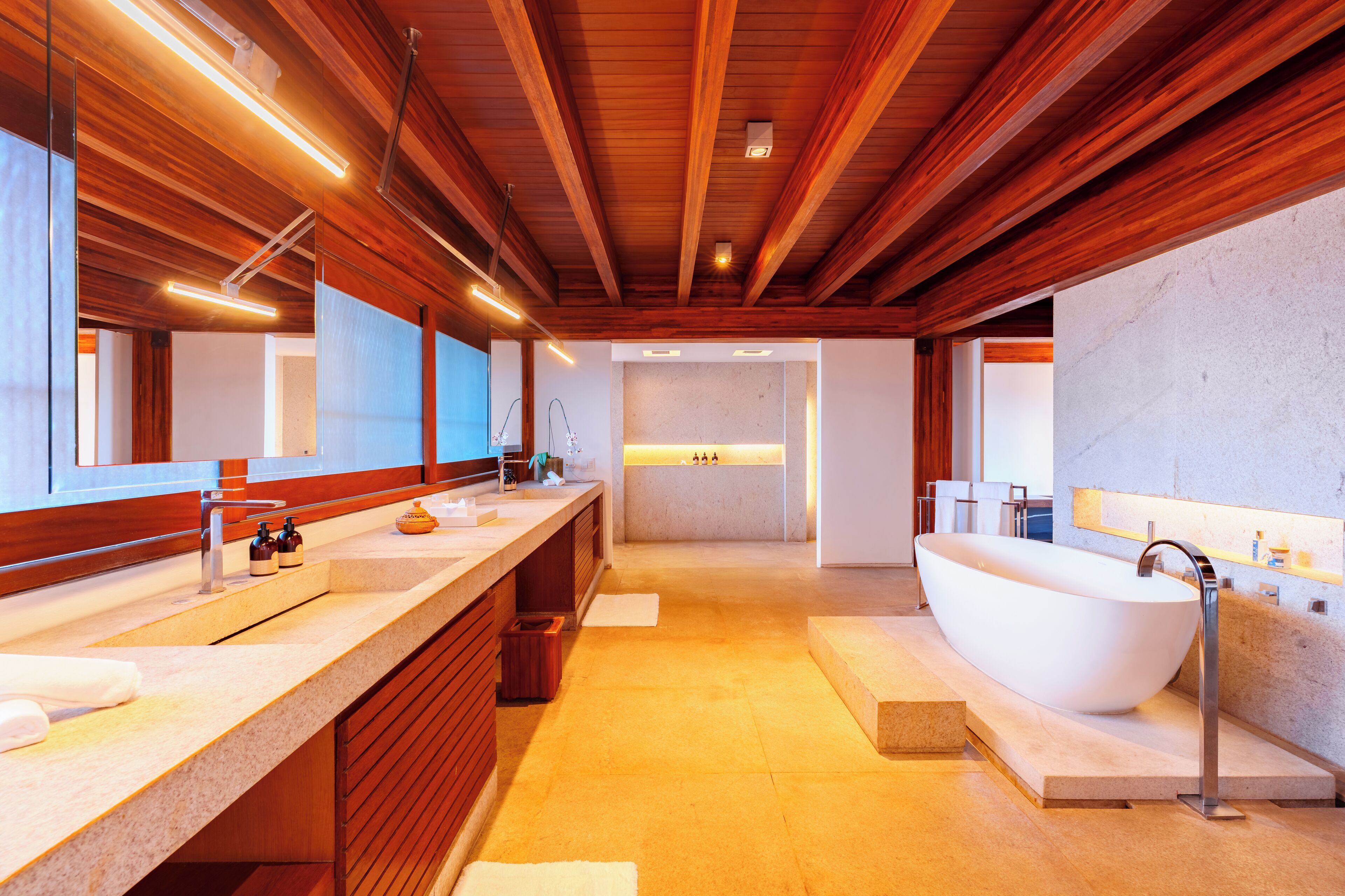 A modern bathroom with wooden beams, a freestanding bathtub, and a large mirror.