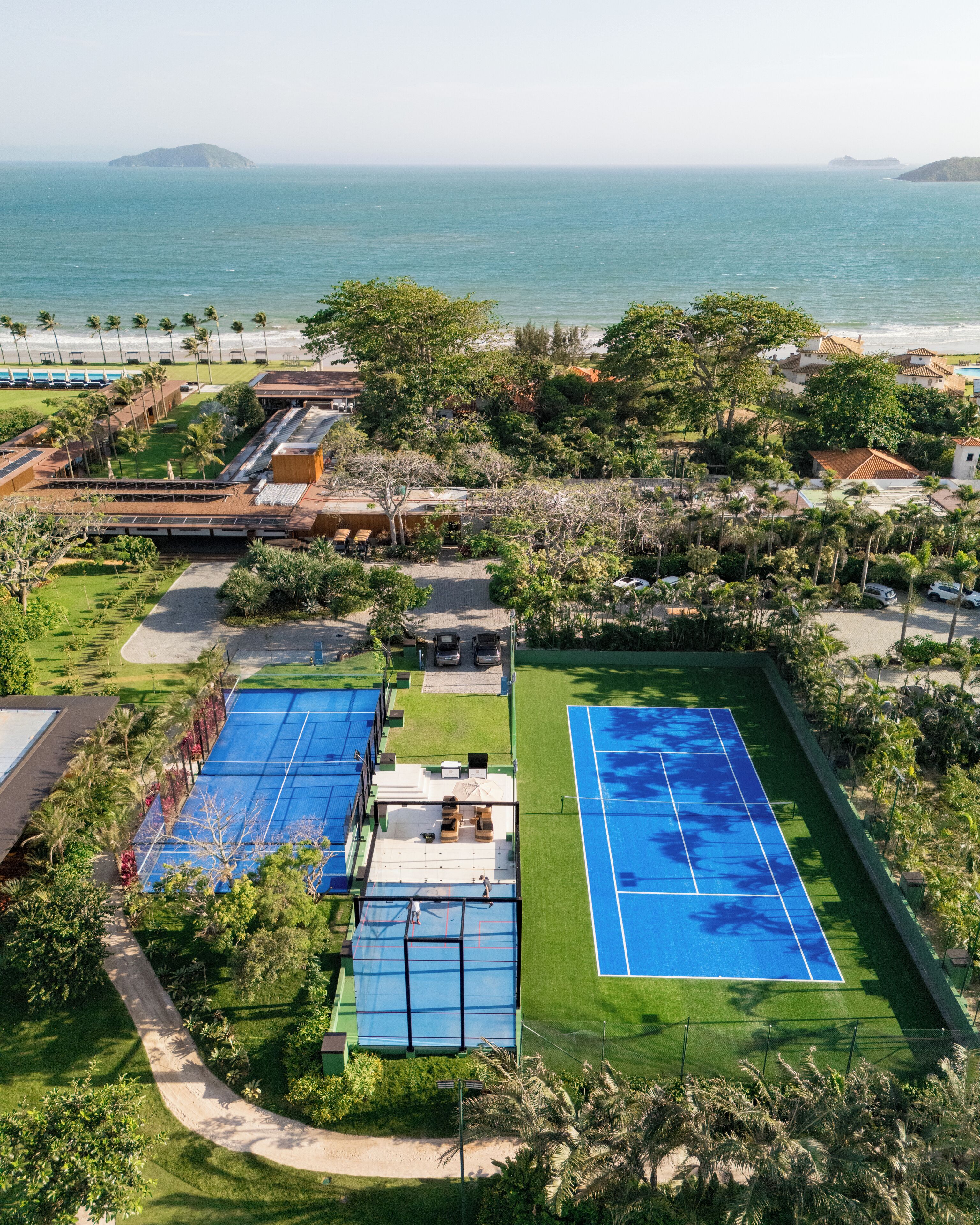 Vista aérea de un resort con varias canchas de tenis, una zona de piscina y vistas al océano.