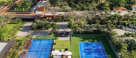 An aerial view of a resort with multiple tennis courts, a pool area, and a view of the ocean.