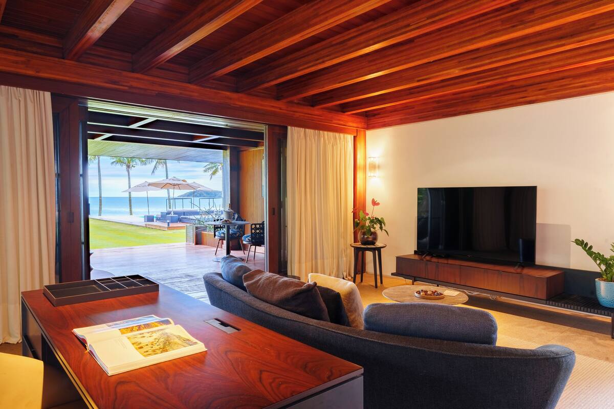 Un salon moderne avec un plafond en bois, un grand téléviseur à écran plat, un canapé et un coin repas comprenant une table et des chaises.