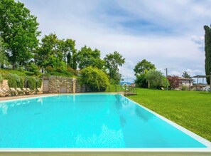 A rectangular swimming pool with clear blue water, surrounded by a well-maintained lawn and trees.