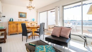 A spacious living room with a large window, a dining area, and a game table. - Les Marinas d'Ulysse IV by Interhome (Port Camargue)