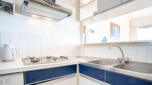 A modern kitchen with white cabinets, a blue accent wall, a gas stove, a sink, and a kettle. - Les Marinas d'Ulysse IV by Interhome (Port Camargue)