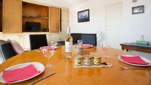 A dining area with a wooden table set for four, surrounded by chairs. There are wine glasses, plates, and a bottle of wine on the table. - Les Marinas d'Ulysse IV by Interhome (Port Camargue)