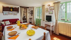A dining area with a table set for four, a television, and a green window with curtains. - La Capannella by Interhome (Camaiore)