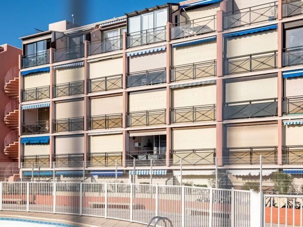 Un hotel de varios pisos con balcones, piscina y entrada con portón.