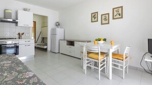 Una cocina moderna con armarios blancos, una estufa y un refrigerador. Hay un comedor con una mesa y sillas blancas.