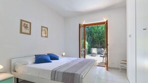 Un dormitorio con una cama, dos cuadros enmarcados, una mesita de noche y vistas a un espacio exterior con sillas.