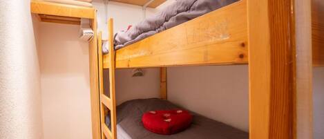 Habitación pequeña con una litera, una escalera corta y una almohada roja en la cama inferior.