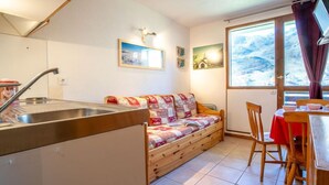 Ein gemütliches Zimmer mit Küchenzeile, einem Holzsofa, einem Esstisch mit Stühlen und einem großen Fenster mit Bergblick.