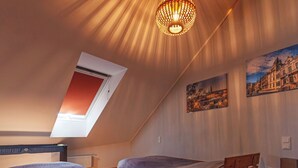 Et soveværelse med to senge i træ, et ovenlysvindue, en hængende lampe og to billeder på væggen.