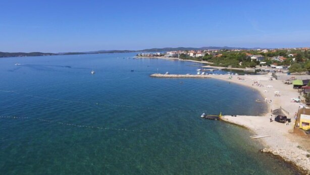 Eine Küstenlandschaft mit klarem, blauem Wasser, einem Sandstrand und einem kleinen Steg.