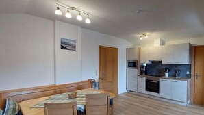 Un espace de vie compact comprenant un coin repas, une kitchenette et un banc en bois avec des coussins.