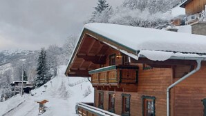 Un chalet en bois doté d’un balcon, entouré d’arbres couverts de neige et avec une montagne en arrière-plan.