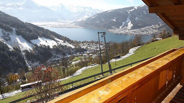 Un balcon offrant une vue sur un paysage montagneux, un lac et une ville au loin.