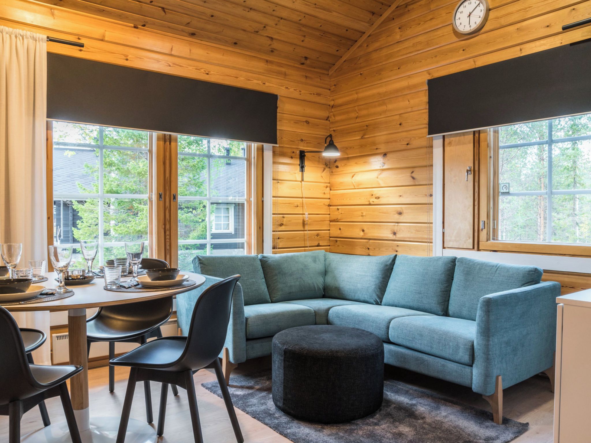 A cozy cabin interior with a dining area, a sofa, and a round ottoman.