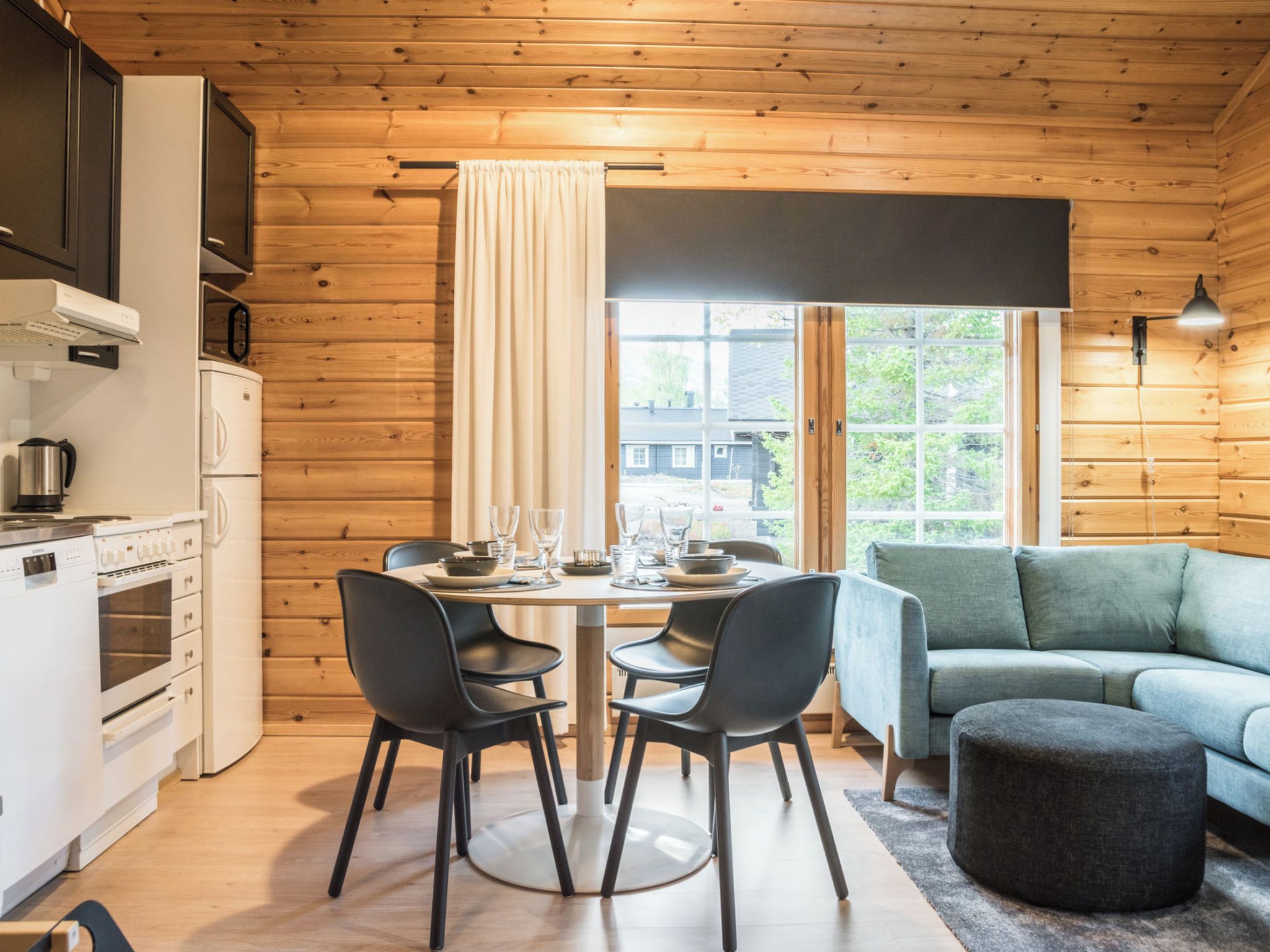Een moderne keuken met witte apparaten, een eethoek met zwarte stoelen en een uitzicht door een raam.