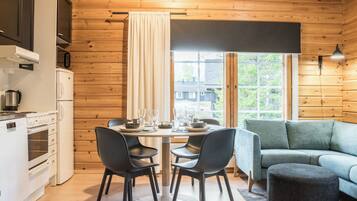Een moderne keuken met witte apparaten, een eethoek met zwarte stoelen en een uitzicht door een raam.