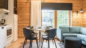 A cozy cabin-style room with a wooden interior, a dining table with chairs, a sofa, and a large window with curtains.