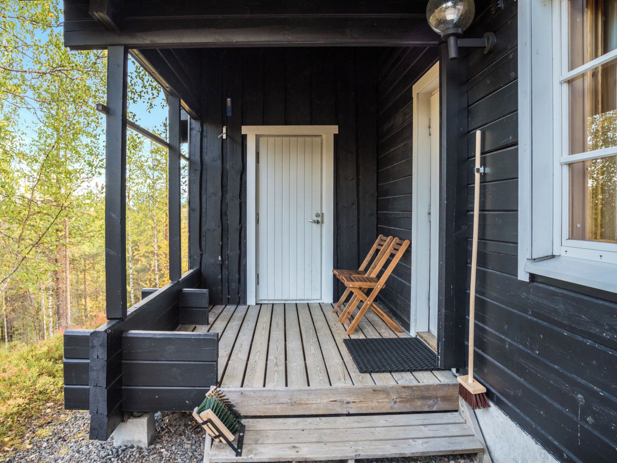 Een houten veranda met een deur, twee houten stoelen en een bezem die tegen de muur staat.