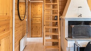 A wooden interior with a central wooden staircase, a fireplace, and a door with a mirror.