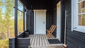 A wooden porch with two wooden chairs, a door, and a window.