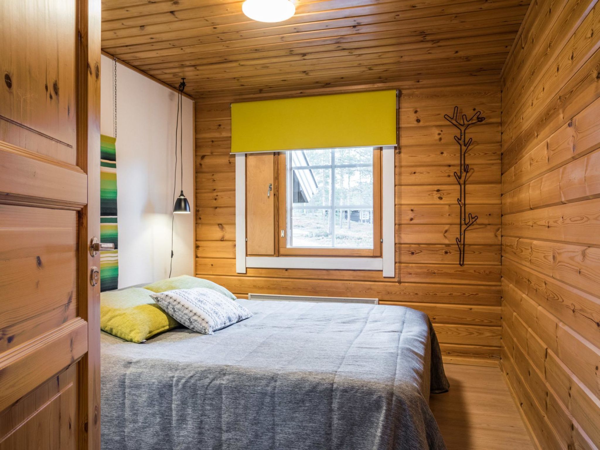 Ein Schlafzimmer in einer Holzhütte mit einem Bett, einem Fenster mit gelbem Rollo und einer Heizung.
