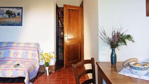 A cozy living room with a sofa, a dining table with chairs, a wooden door, a bookshelf, and a vase with flowers. - Pulcino n°3 by Interhome (Gaiole in Chianti)