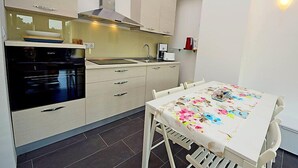 Une cuisine moderne équipée d’un four encastré, d’une cuisinière et d’un évier. On y trouve une table à manger avec une nappe à motifs floraux et des chaises.
