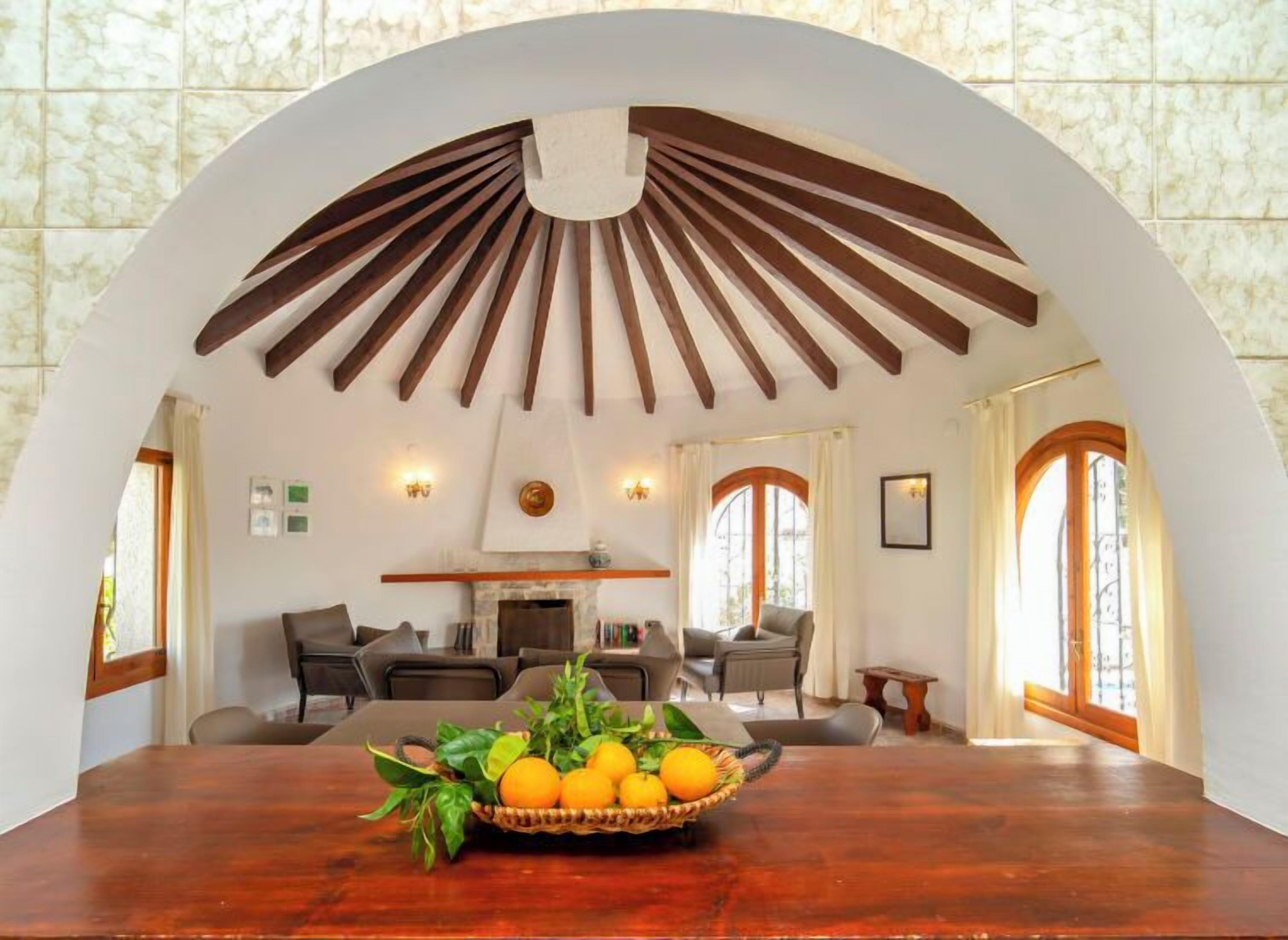 A dining area with a wooden table, a basket of fruit, and a fireplace.