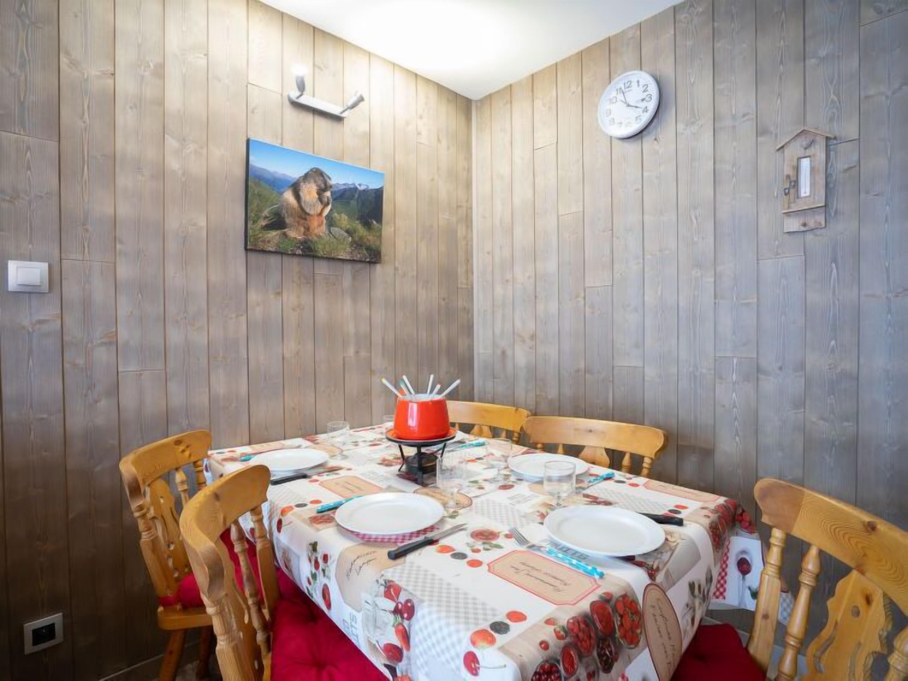 A dining area with a wooden paneled wall, a painting, a clock, and a table set with plates and cutlery.
