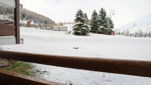 Un espace extérieur enneigé avec des bancs en bois, un bâtiment rouge et des arbres couverts de neige.
