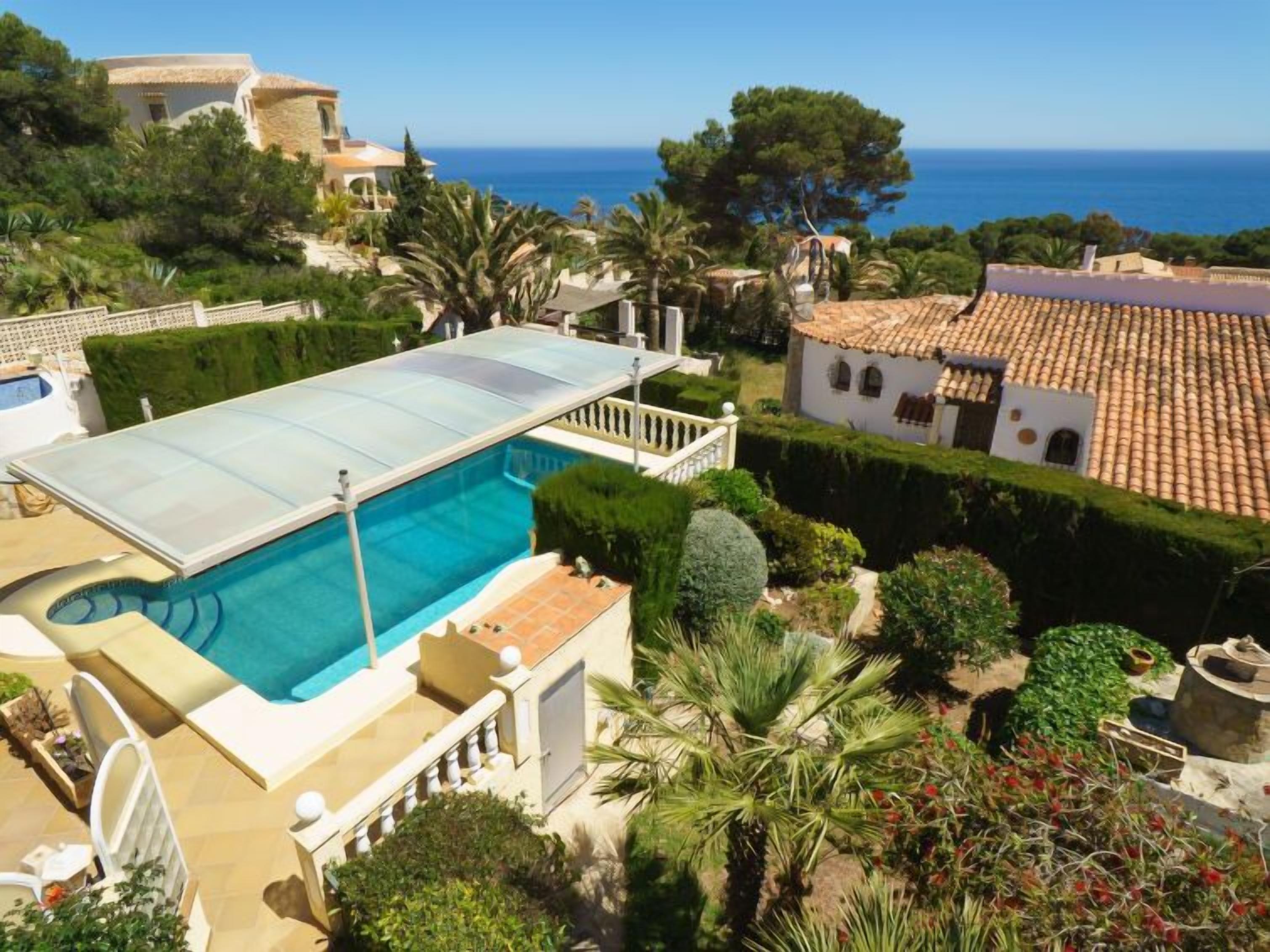 Piscina com cobertura de vidro, rodeada por vegetação exuberante e arquitetura em estilo mediterrâneo.
