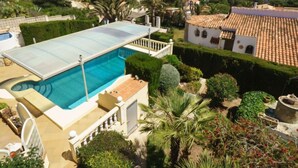 Una piscina con cerramiento de vidrio, rodeada de exuberante vegetación y arquitectura de estilo mediterráneo.