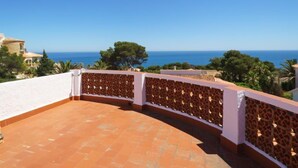 Una terraza curva con un enrejado decorativo, con vistas a un paisaje costero con árboles y un cielo azul despejado.
