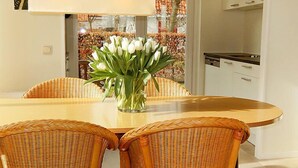 Un comedor con una mesa redonda, sillas de mimbre y un jarrón de flores blancas.